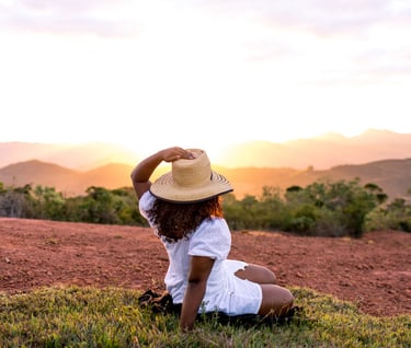 a woman in a white shirt and hat sitting on a hill