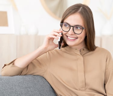 a woman in glasses and a brown shirt is talking on the phone
