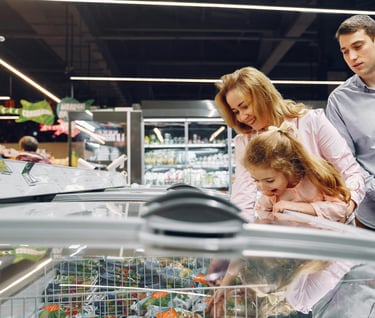 A family choosing frozen food from a grocery store freezer aisle while grocery shopping together.