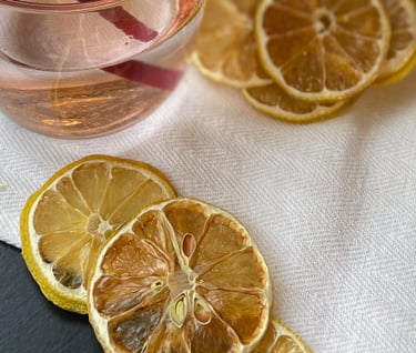 dehydrated lemons displayed in and around pink water glass with metal straw in front of plants
