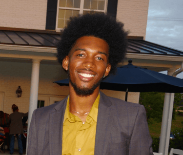 Kelvin in a suit and yellow shirt standing in front of a house