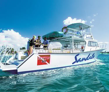 Scuba divers preparing for a dive on a Sandals luxury resort boat in tropical turquoise waters.
