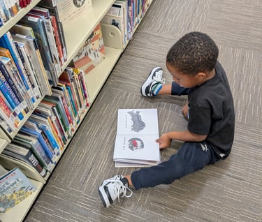 little boy sitting on the floor reading a book in the library