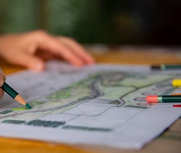 dizainerė laiko pieštuką ir spalvina kraštovaizdžio eskizą