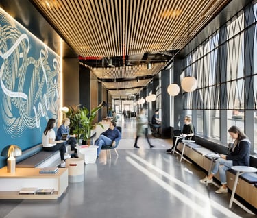 Modern office breakout area with wood slat ceilings, mural wall, and people working in a bright lounge.