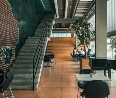 Modern industrial cafe interior with concrete stairs, brick walls, and people sitting at tables.