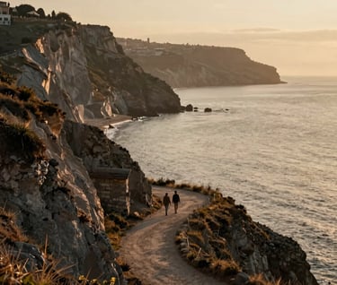 A large, cinematic landscape of a Southern European / Italian coastline during the golden hour. A couple is seen from a distance walking along a cliffside path. The atmosphere is hazy, warm, and deeply romantic, featuring sand and anthracite tones.