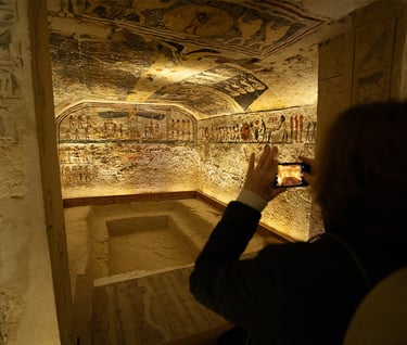 Tourist taking a photo of ancient Egyptian hieroglyphics and wall paintings inside a stone tomb.