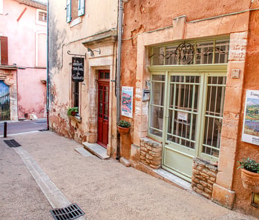 Quaint art gallery and studio along a narrow street with terracotta walls in Roussillon, France.