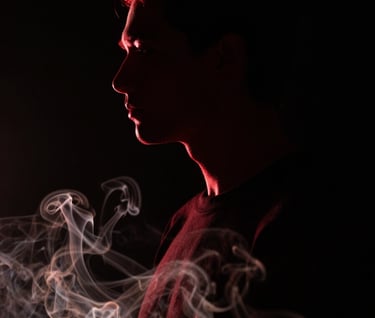 A cinematic portrait of a person in shadow, only their silhouette is visible against a deep black background. A thin rim light in vivid deep red outlines their profile, while subtle off-white smoke swirls in the foreground.