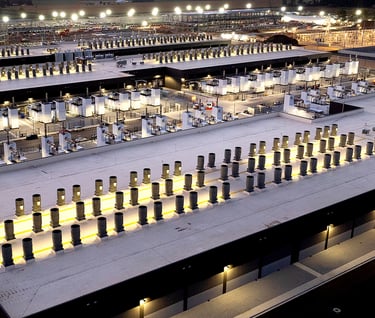 Aerial night view of a large-scale data center facility with industrial cooling systems and illuminated infrastructure.