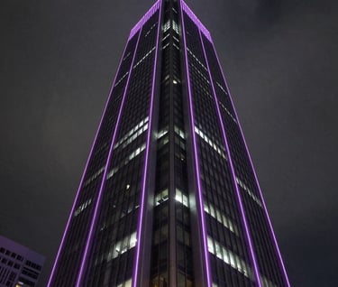 A low-angle, impactful shot of a modern skyscraper in a North American metropolitan area at night. The building is lit with sharp lavender neon lines against a dark grey sky, conveying a powerful and mysterious corporate presence.