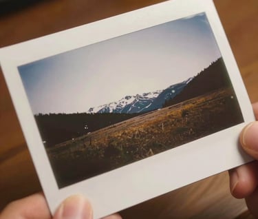 A close-up shot of a high-quality, matte-finish photographic print being held by hands, showing a minimalist North American / Canadian landscape, soft off-white borders, warm indoor lighting.