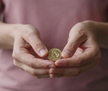 A close-up photograph of a person's hands in a modern International / Western setting, carefully holding a clean, golden coin. The focus is sharp on the metallic texture, with the background softly blurred in shades of Dusty Rose Petal and Deep Plum Twilight.
