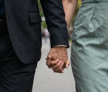 An artistic close-up of a couple's hands intertwined while walking through a North American / US city park. The lighting is soft and professional. The focus is on the intimacy and the elegant textures of their clothing in Dark Charcoal and Sage Green.