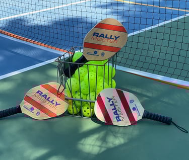 Three Rally Meister wooden pickleball paddles leaning against a metal basket filled with neon yellow pickleballs on a court.