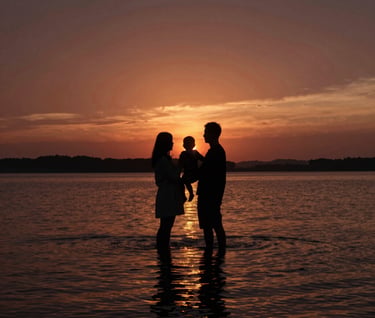A cinematic landscape shot featuring a family silhouette against a deep terracotta sunset over a lake. The reflection on the water is shimmering with charcoal and gold highlights. The composition is expansive and storytelling-focused.