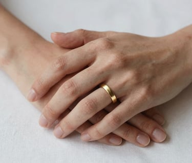 Close-up of two hands intertwined, featuring a brushed gold engagement ring, set against a clean white linen background, North American / US setting, soft luxe lighting.