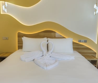 Luxury hotel bed with white swan towel art, warm LED backlighting, and modern yellow wall decor.