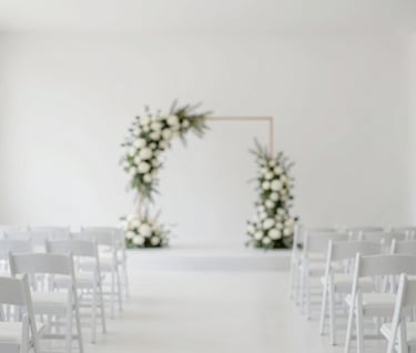 Wide shot of a modern, minimalist wedding ceremony aisle with white chairs and simple floral arrangements, bright and airy atmosphere, dominated by #FDFDFD with #A39E97 accents.