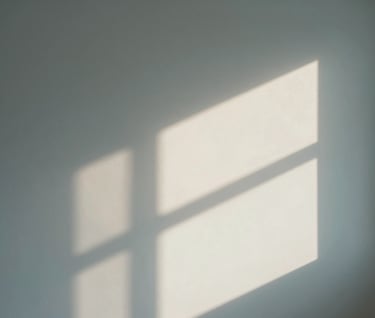 Conceptual interior photography of a minimalist room. A single ray of light hits an off-white wall, creating sharp geometric shadows. Soft slate blue tones in the shadows.