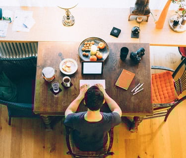 A top-down view of a writer working at a wooden table with a laptop, notebook, coffee, and snacks, surrounded by creative too