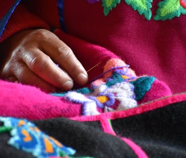 mano de una artesana con una aguja bordando una flor en un paño rosado