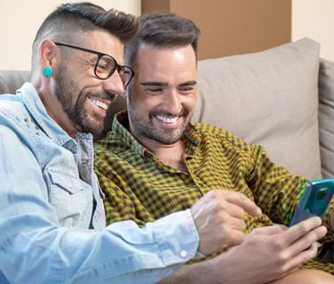 two men sitting on a couch looking at their phones