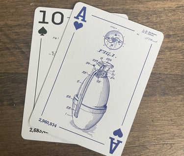 Two playing cards faced up. A close up view of a blue grenade engineering drawing is shown