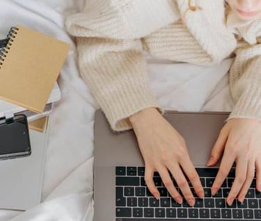 a woman sitting on a bed with a laptop and notebook