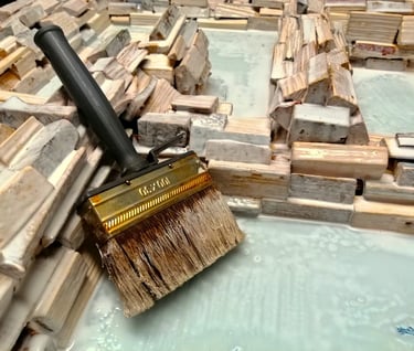 Foto eines großen Pinsels nach dem Einstreichen eines Spiegelrahmens aus unzähligen, naturbelassenen Holzscheiten