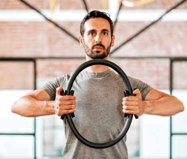 Man with brown hair using a pilates magic ring to exercise his arms.
