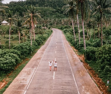 two people walking down a road with palm trees
