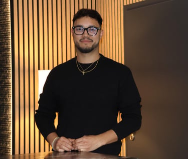 Professional man with glasses and black sweater standing against a modern wood slat wall.