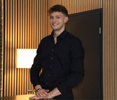 Smiling professional man in black dress shirt posing against a modern wood-slat wall background.