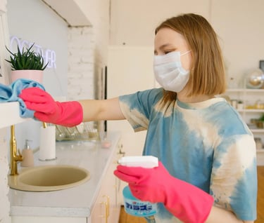 a woman in a mask and gloves is cleaning a sink