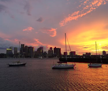 a sunset over a cityscape with boats in the water in Bostonater