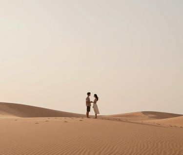 A wide-angle cinematic shot of a couple standing together on a sand dune under a vast, soft sky. The palette consists of warm sand #FDF8F0 and soft terracotta #AD7B5B hues. Authentic, quiet interaction.