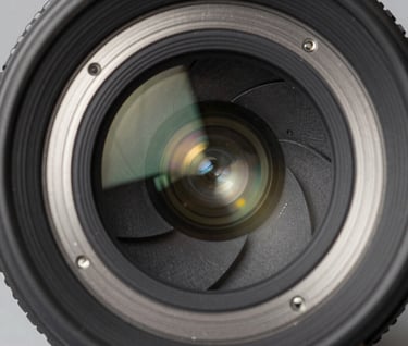 A macro close-up of a premium camera lens, showing the intricate aperture blades and multi-coated glass elements, reflecting soft light, industrial and clean aesthetic, slate and silver tones.