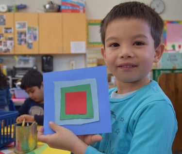 a boy holding a square shaped paper cutout
