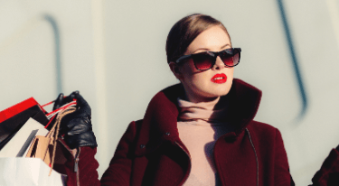 a woman in a red coat and sunglasses holding shopping bags