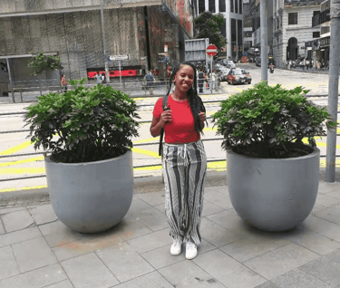 a woman standing on a sidewalk next to a large potted planter