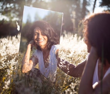 woman looking at herself in mirror while sitting in open field