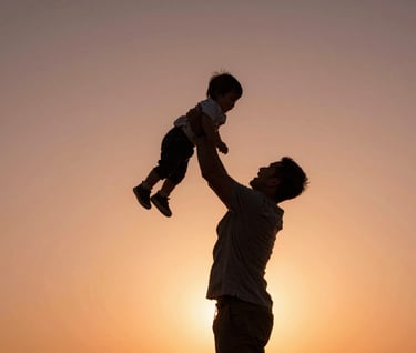 A father lifting his toddler into the air, back-lit by the setting sun in a North American / General Western park. Silhouette effect with a warm terracotta glow against a soft sand background.