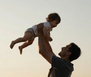 A father lifting a toddler high into the air against a clear, soft off-white sand sky. The composition is a low-angle silhouette with warm golden light outlining their shapes. Cinematic and evocative.