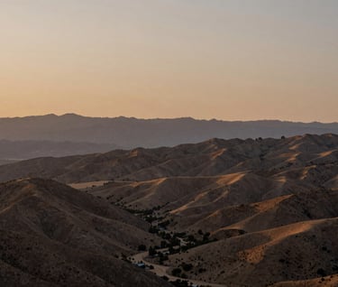 A wide cinematic landscape of an Ojai valley at dusk, hazy soft sand colored sky meeting earthy brown mountains, peaceful and authentic atmosphere.