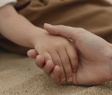 A close-up detail shot of a mother's hand holding her child's hand, warm soft sand skin tones, earthy brown fabric in the background, cinematic soft lighting.