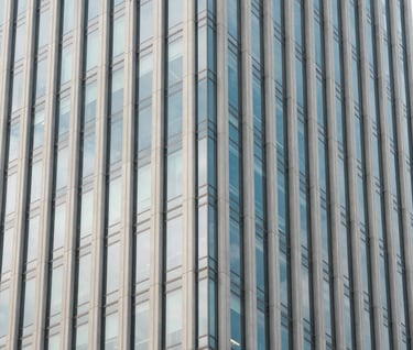 A minimalist architectural detail of a glass skyscraper in a North American city reflecting a pale blue sky. Clean lines, contemporary design, off-white and soft blue-grey tones.