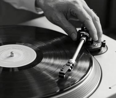 Macro photography of a professional's hands on a vinyl turntable in a Spanish / Latin American venue. Monochrome style with soft platinum highlights on obsidian surfaces. Motion blur on the record, elegant and experienced movement.