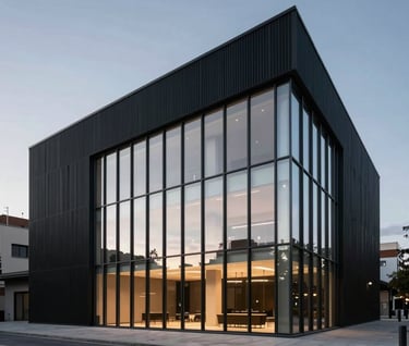 Minimalist architectural photography of a modern concert hall exterior in a Spanish / Latin American metropolis at dusk. Clean lines, night black facade with soft silver glow from the floor-to-ceiling windows.